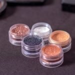 Variety of glitter eyeshadows in small containers on a dark background.