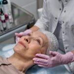 A mature woman in a spa receiving a relaxing facial treatment from a professional in a medical clinic setting.